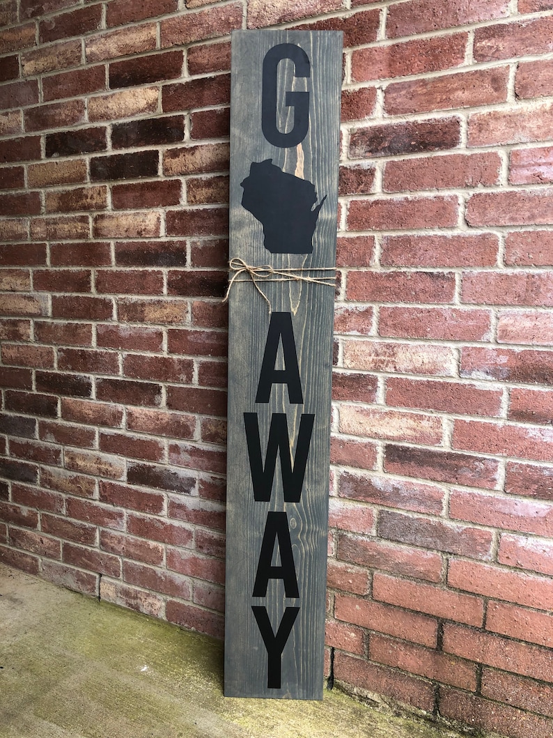 May include: A wooden sign with the word "G" and the outline of the state of Wisconsin, followed by the word "AWAY" spelled vertically. The sign is painted gray with black lettering.