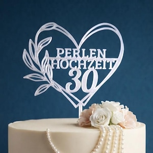 Może przedstawiać: Biały topper na tort w kształcie serca z motywem liści i napisem PERLEN HOCHZEIT 30, umieszczony na okrągłym białym torcie ozdobionym sznurami białych pereł oraz bukietami białych i jasnor&oacute;żowych r&oacute;ż.