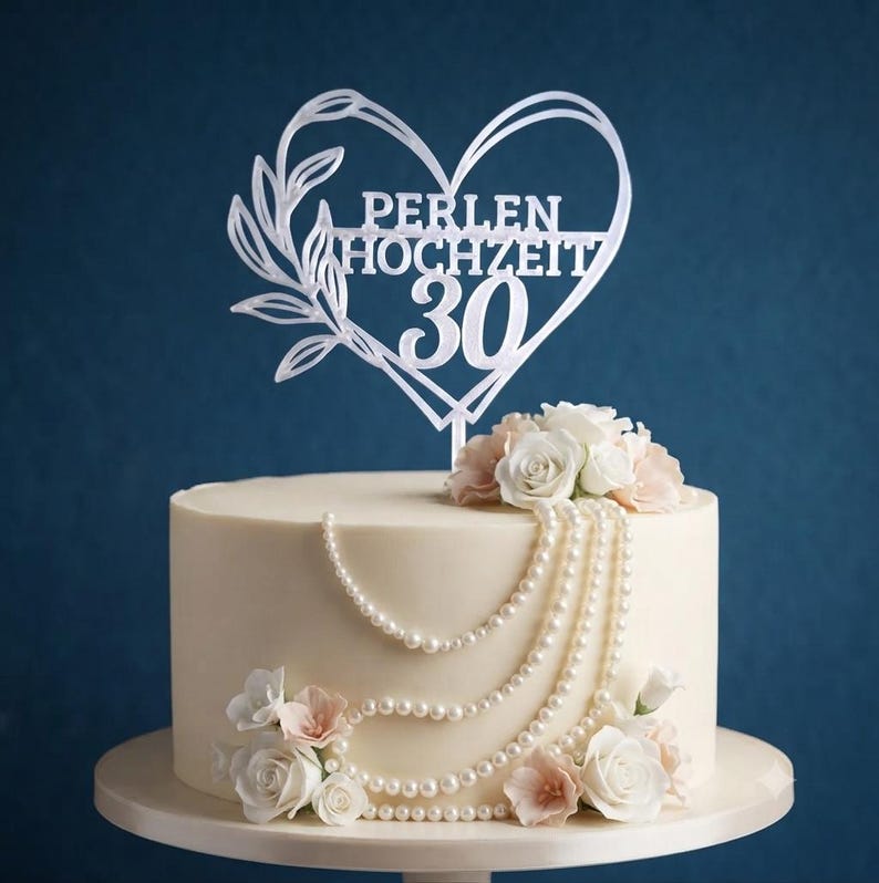 Może przedstawiać: Biały topper na tort w kształcie serca z motywem liści i napisem PERLEN HOCHZEIT 30, umieszczony na okrągłym białym torcie ozdobionym sznurami białych pereł oraz bukietami białych i jasnor&oacute;żowych r&oacute;ż.