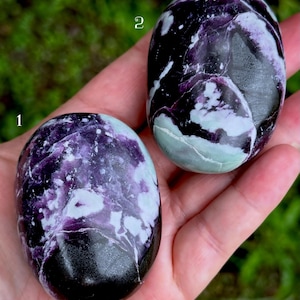 May include: Two polished, oval-shaped stones featuring deep purple, black, and white marbled patterns. The stone labeled 1 is positioned lower, while the stone labeled 2 is positioned higher. Both stones have a smooth, glossy surface texture.
