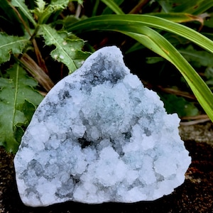 May include: A triangular-shaped mineral geode featuring a cluster of small, translucent, pale blue and white crystalline structures. The interior cavity is densely packed with sparkling, jagged crystal formations that taper toward a pointed top.