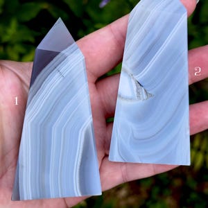 May include: Two polished blue lace agate crystal towers with distinct white and light blue banding patterns. The stone labeled 1 is shorter with a sharp point, while the stone labeled 2 is taller and features a small internal crystalline cavity.