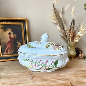 May include: White porcelain serving dish with a floral design featuring pink, yellow, and green flowers. The dish has a gold rim and a lid with a floral knob.