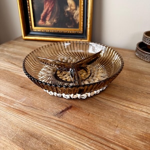 May include: A brown glass divided serving dish with a fluted design and a clear glass base. The dish has three sections and a central handle.
