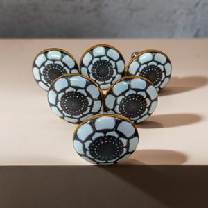 May include: Set of seven white ceramic cabinet knobs with a black and gold floral design.