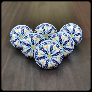 Op de afbeelding: Zes keramische knoppen met een blauw, wit, geel en rood bloemenpatroon. De knoppen zijn rond en hebben een verhoogde rand.