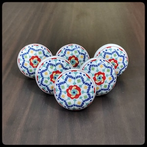 Op de afbeelding: Zes keramische knoppen met een witte achtergrond en een kleurrijk geometrisch patroon in tinten blauw, rood, geel en groen.