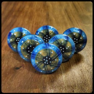 Op de afbeelding: Vijf blauwe en gouden keramische kastknoppen met een geometrisch ontwerp in zwart en wit. De knoppen zijn rond en hebben een verhoogde rand.