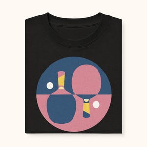 K&ouml;nnte beinhalten: Schwarzes Sweatshirt mit einer Grafik von Tischtennisschl&auml;gern und -b&auml;llen in einem blau-rosa Kreis. Die Schl&auml;ger haben gelbe und wei&szlig;e Details. Das Design ist auf dem gefalteten Kleidungsst&uuml;ck zentriert.
