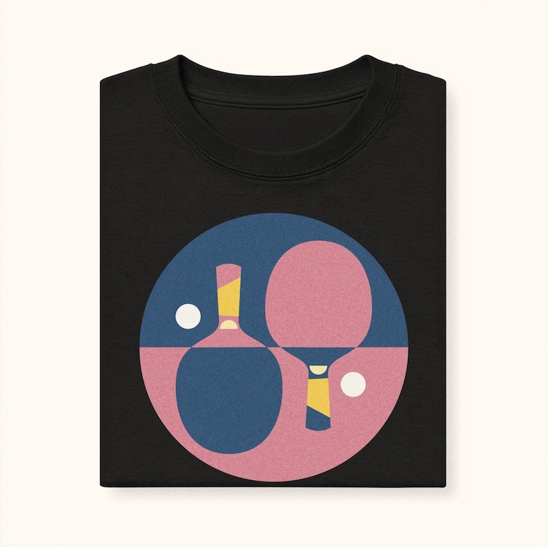 K&ouml;nnte beinhalten: Schwarzes Sweatshirt mit einer Grafik von Tischtennisschl&auml;gern und -b&auml;llen in einem blau-rosa Kreis. Die Schl&auml;ger haben gelbe und wei&szlig;e Details. Das Design ist auf dem gefalteten Kleidungsst&uuml;ck zentriert.