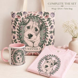 May include: A pink mug, t-shirt, and tote bag set featuring a dog portrait within a floral wreath. The tote bag and t-shirt are light pink, while the mug has a pink interior and handle. The word "WINNIE" is printed on each item.