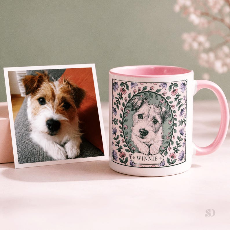 May include: A white ceramic mug with a pink interior and handle, featuring a dog portrait surrounded by a floral wreath. A photograph of the same dog is next to the mug. The mug has the name "Winnie" on it.