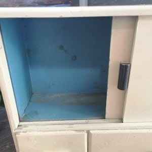 May include: A white vintage cabinet with a sliding door and three drawers. The inside of the cabinet is painted a light blue color.