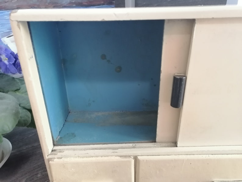May include: A white vintage cabinet with a sliding door and three drawers. The inside of the cabinet is painted a light blue color.