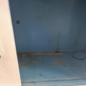May include: The inside of a metal locker with a light blue paint finish. The locker has some dirt and grime on the bottom and sides.