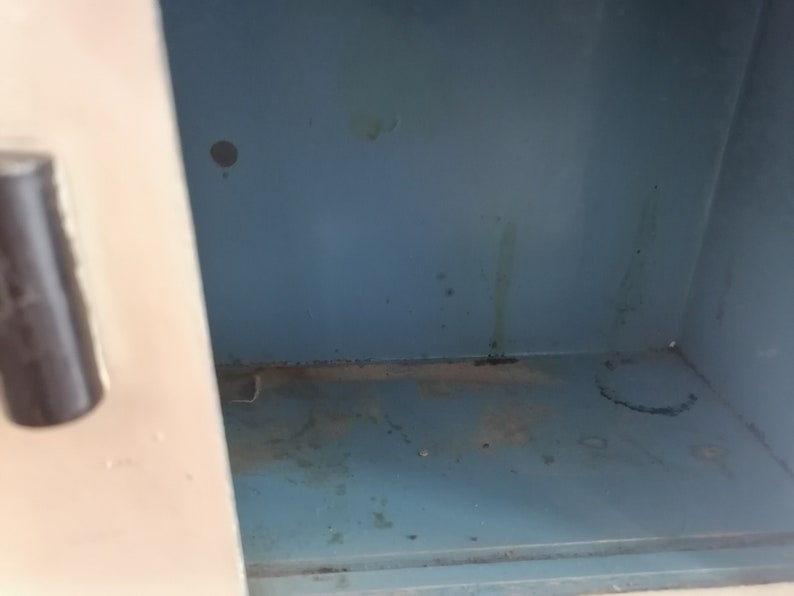 May include: The inside of a metal locker with a light blue paint finish. The locker has some dirt and grime on the bottom and sides.