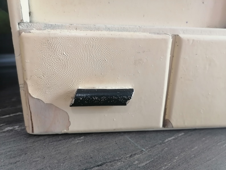 May include: A white wooden cabinet with a black handle. The cabinet has a textured surface and is slightly chipped.