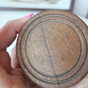 Puede incluir: Primer plano de un objeto redondo de madera con acabado marr&oacute;n oscuro. El objeto tiene c&iacute;rculos conc&eacute;ntricos tallados en su superficie, con vetas de madera visibles y una l&iacute;nea oscura que atraviesa el centro.