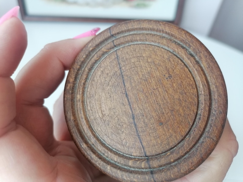 Puede incluir: Primer plano de un objeto redondo de madera con acabado marr&oacute;n oscuro. El objeto tiene c&iacute;rculos conc&eacute;ntricos tallados en su superficie, con vetas de madera visibles y una l&iacute;nea oscura que atraviesa el centro.