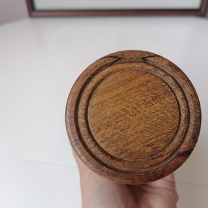 Puede incluir: Primer plano de un objeto de madera con un dise&ntilde;o circular. El objeto es de color marr&oacute;n claro con una superficie texturizada. La parte superior tiene un &aacute;rea circular empotrada. El objeto se sostiene en una mano.