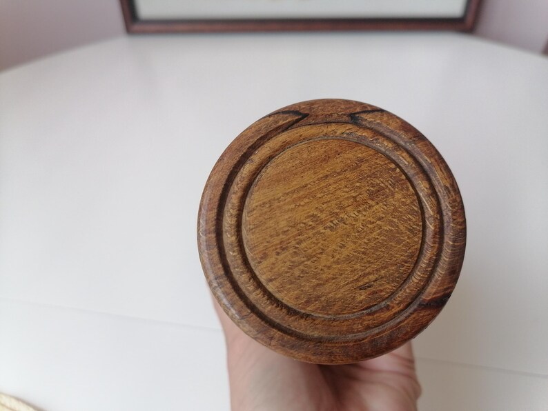 Puede incluir: Primer plano de un objeto de madera con un dise&ntilde;o circular. El objeto es de color marr&oacute;n claro con una superficie texturizada. La parte superior tiene un &aacute;rea circular empotrada. El objeto se sostiene en una mano.