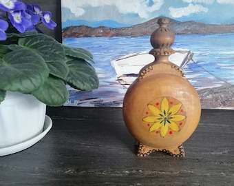 Könnte beinhalten: Eine Holzflasche mit einer gelben Blume, die auf die Vorderseite gemalt ist. Die Flasche hat einen Holzverschluss und steht auf drei Beinen.
