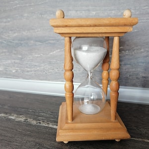 Könnte beinhalten: Eine Sanduhr aus Holz mit weißem Sand im Inneren. Die Sanduhr steht auf einer dunkelgrauen Arbeitsplatte.