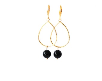 May include: A pair of gold-colored teardrop earrings with a textured finish. Each earring features a faceted black bead suspended from the bottom. The earrings are displayed against a white background.