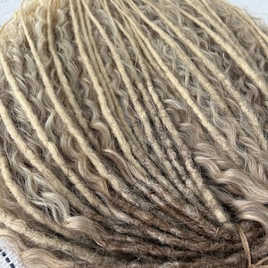 May include: A bundle of blonde and light brown synthetic dreadlocks. The dreadlocks are wavy and have a natural, textured look.