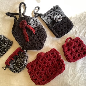 May include: A collection of handmade crochet bags and pouches in various colors. The bags include a dark gray tote with a red bow, a red pouch, and a gray and black pouch. The crochet work is visible.