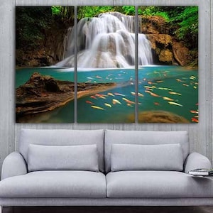 May include: A three-panel canvas print featuring a verdant waterfall cascading into a pool of water teeming with colourful fish. The waterfall is surrounded by tropical foliage and a large rock formation.