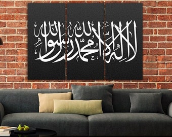 May include: A triptych canvas art piece with white Arabic calligraphy on a textured black background. The artwork hangs above a gray sofa with decorative pillows. The background is a red brick wall, and a black floor lamp and side tables are in the foreground.