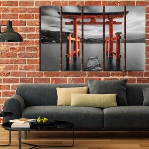 May include: A black and white photograph of a red Japanese Torii gate, a traditional gateway, standing in a body of water. The gate is partially submerged in the water, and the water is calm and reflective. The sky is cloudy and overcast.
