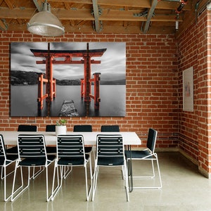 May include: A black and white photograph of a red Japanese Torii gate, a traditional gateway, standing in a body of water. The gate is surrounded by water and a small path leads to it.