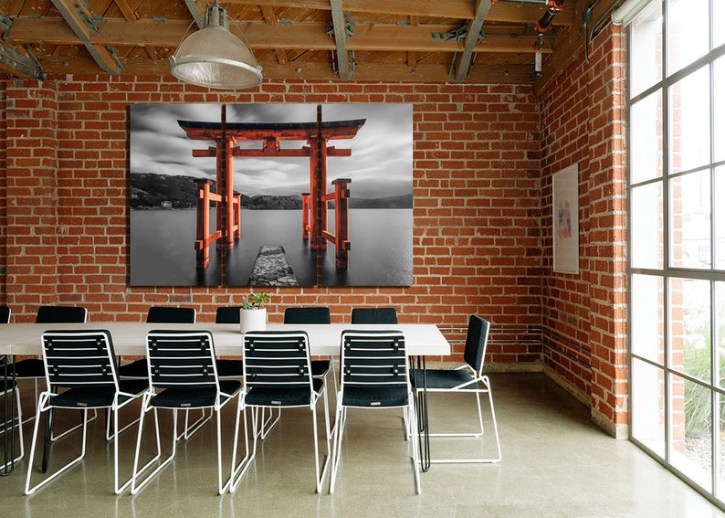 May include: A black and white photograph of a red Japanese Torii gate, a traditional gateway, standing in a body of water. The gate is surrounded by water and a small path leads to it.
