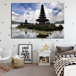 May include: A black temple with a tiered roof sits on a small island in a lake. The temple is surrounded by lush greenery and the water is calm and reflective. The sky is blue with white clouds.