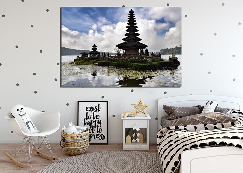 May include: A black temple with a tiered roof sits on a small island in a lake. The temple is surrounded by lush greenery and the water is calm and reflective. The sky is blue with white clouds.