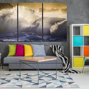 May include: A living room interior design with a gray sofa, a coffee table, a white chair, a green chair, a bookshelf with colorful boxes, and a large canvas print of crashing ocean waves.