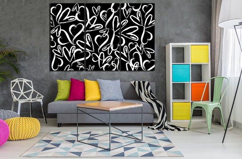 Puede incluir: Un interior de sala de estar con un sof&aacute; gris, una silla blanca, una silla verde, una mesa de caf&eacute; de madera y una estanter&iacute;a blanca con contenedores de almacenamiento coloridos. Una impresi&oacute;n de lienzo en blanco y negro con un patr&oacute;n de corazones blancos sobre un fondo negro cuelga de la pared.