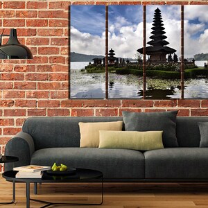 May include: A three-panel canvas print featuring a traditional Balinese temple on a lake. The temple is a multi-tiered structure with a dark wood roof and intricate carvings. The lake is calm and reflective, with a blue sky and white clouds in the background.