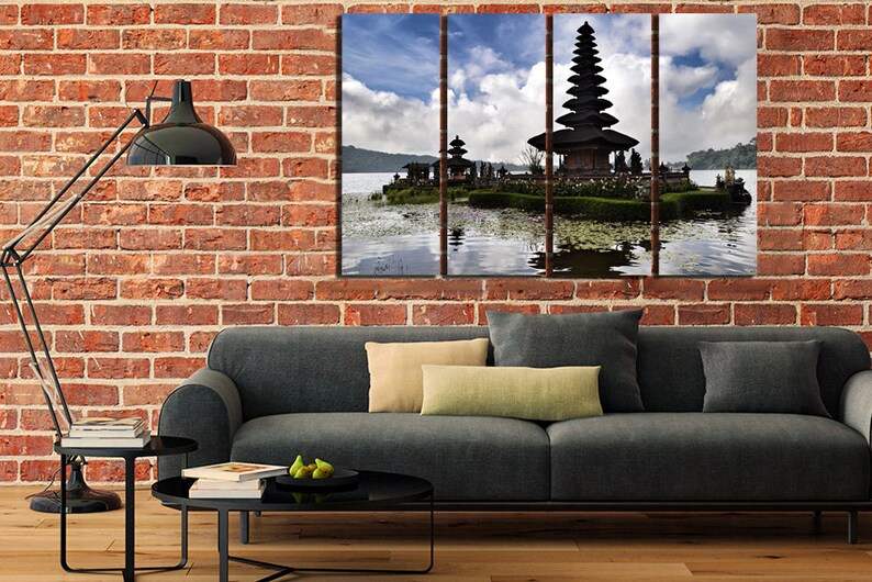 May include: A three-panel canvas print featuring a traditional Balinese temple on a lake. The temple is a multi-tiered structure with a dark wood roof and intricate carvings. The lake is calm and reflective, with a blue sky and white clouds in the background.