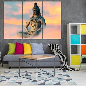 May include: A tri-panel canvas print featuring a colorful sunset sky with a meditating Shiva statue in the center. The statue is blue and gold with a beaded necklace and a serene expression.