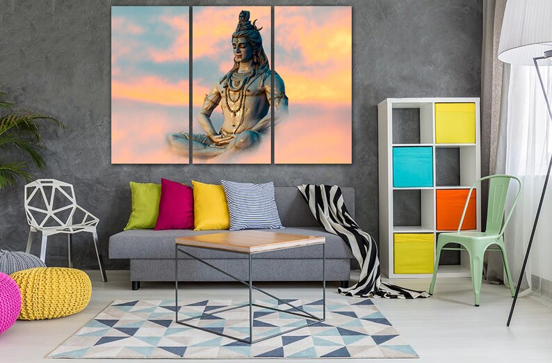 May include: A tri-panel canvas print featuring a colorful sunset sky with a meditating Shiva statue in the center. The statue is blue and gold with a beaded necklace and a serene expression.