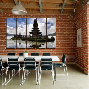 May include: A three-panel canvas print featuring a scenic view of a traditional Balinese temple on a small island in a lake. The temple is surrounded by lush greenery and the water reflects the sky and clouds.