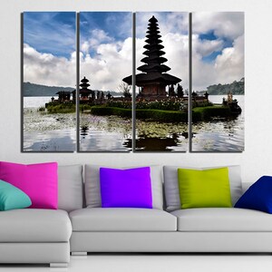 May include: A multi-panel canvas print featuring a traditional Balinese temple on a lake. The temple is a tiered structure with a thatched roof and intricate carvings. The lake is calm and reflective, with lily pads floating on the surface. The sky is blue with white clouds.