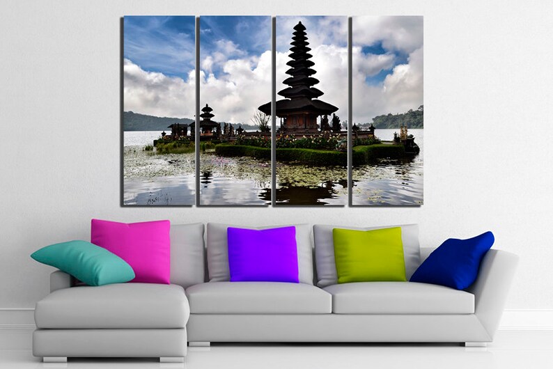 May include: A multi-panel canvas print featuring a traditional Balinese temple on a lake. The temple is a tiered structure with a thatched roof and intricate carvings. The lake is calm and reflective, with lily pads floating on the surface. The sky is blue with white clouds.