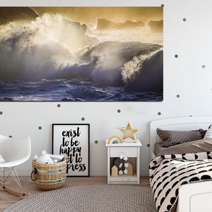 May include: A photograph of crashing waves in a golden light. The waves are crashing against a rocky shore. The water is a deep blue and the sky is a light blue. The sun is shining brightly and the waves are sparkling.