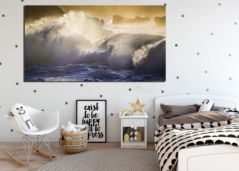 May include: A photograph of crashing waves in a golden light. The waves are crashing against a rocky shore. The water is a deep blue and the sky is a light blue. The sun is shining brightly and the waves are sparkling.