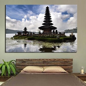 May include: A black and white photograph of a traditional Balinese temple on a small island in a lake. The temple has a tiered roof and is surrounded by lush greenery. The sky is blue with white clouds.