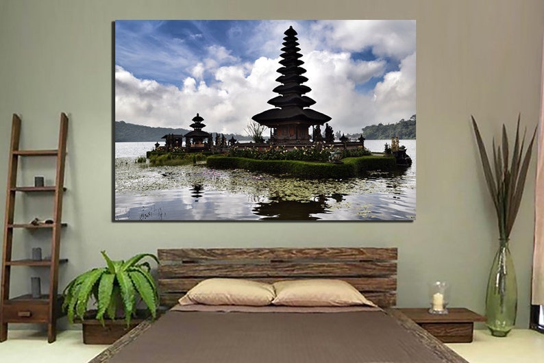 May include: A black and white photograph of a traditional Balinese temple on a small island in a lake. The temple has a tiered roof and is surrounded by lush greenery. The sky is blue with white clouds.